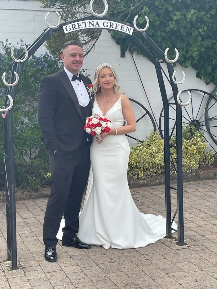 bride and groom under gretna green arch with red faux bridal flowers created by the brides bouquet uk
