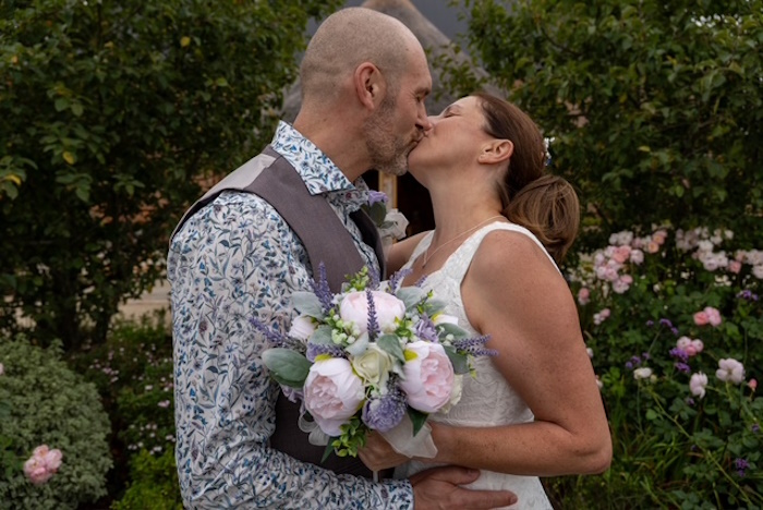 real life bride and groom kissing with silk peony and heather bridal bouquet